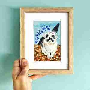 Framed rabbit art being held up against a blue wall