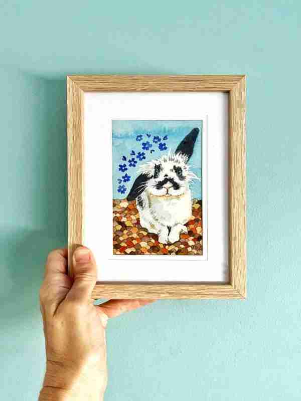 Framed rabbit art being held up against a blue wall