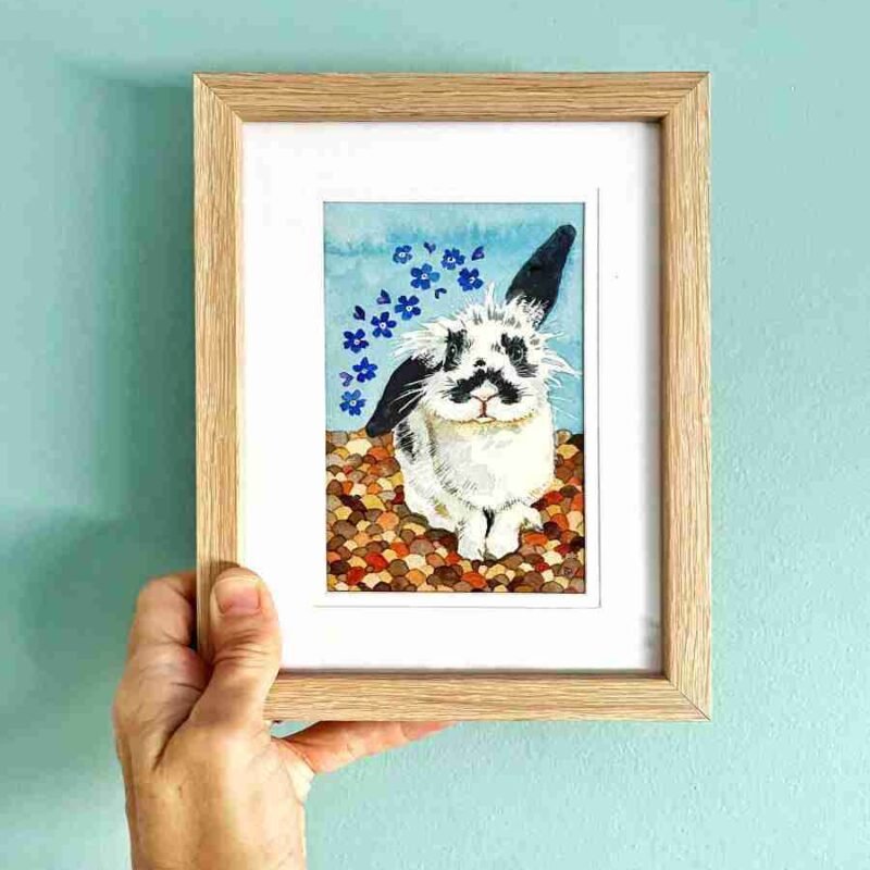 Framed rabbit art being held up against a blue wall
