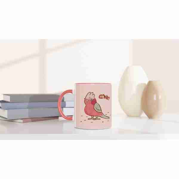 Pink mug with galah bird design on a shelf with books and ornaments