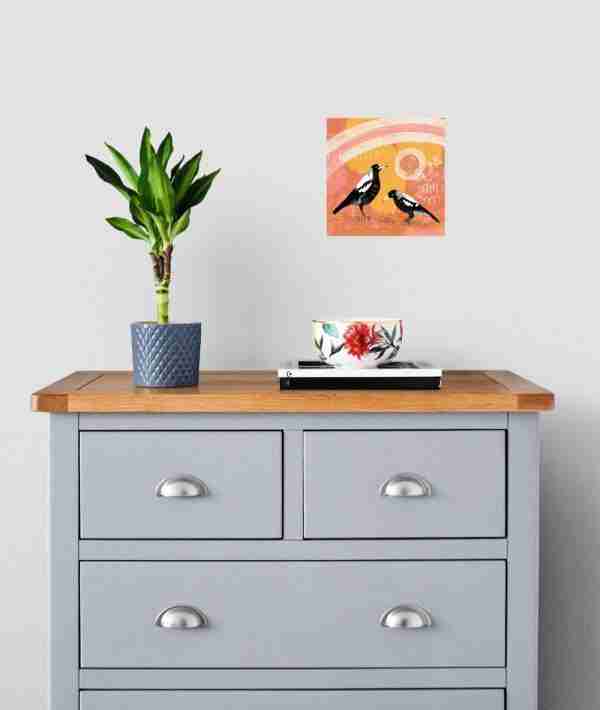 Australian magpies art print above a grey wood cabinet with a plant and ornament